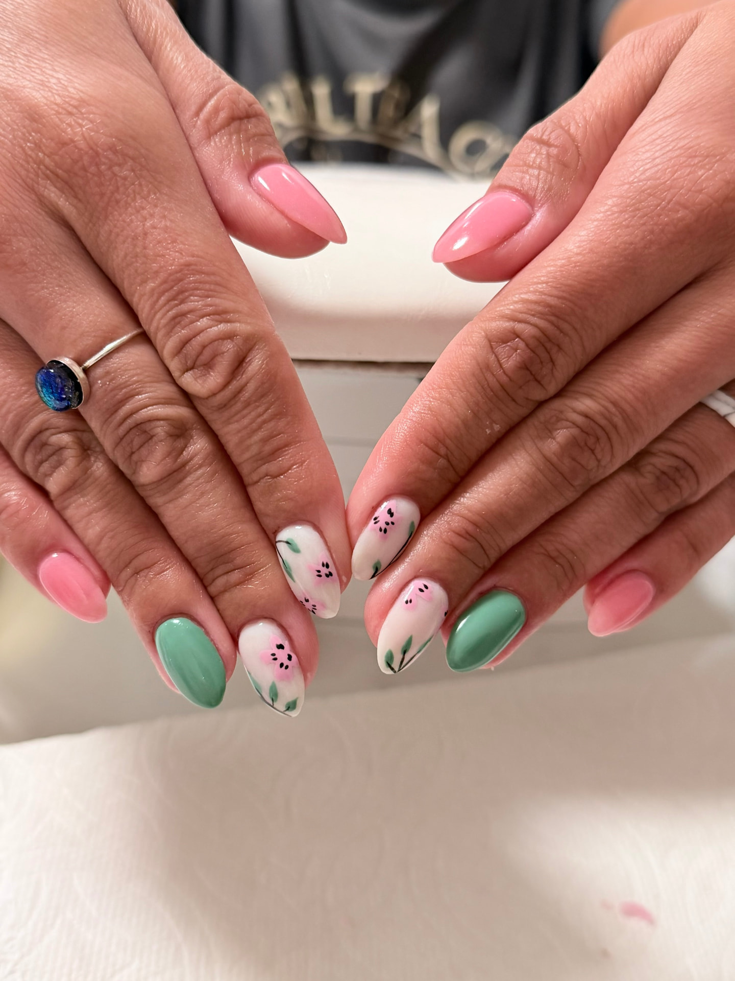 Pink, sage green and sheer almond nails with hand-painted black and pink flowers and green leaves