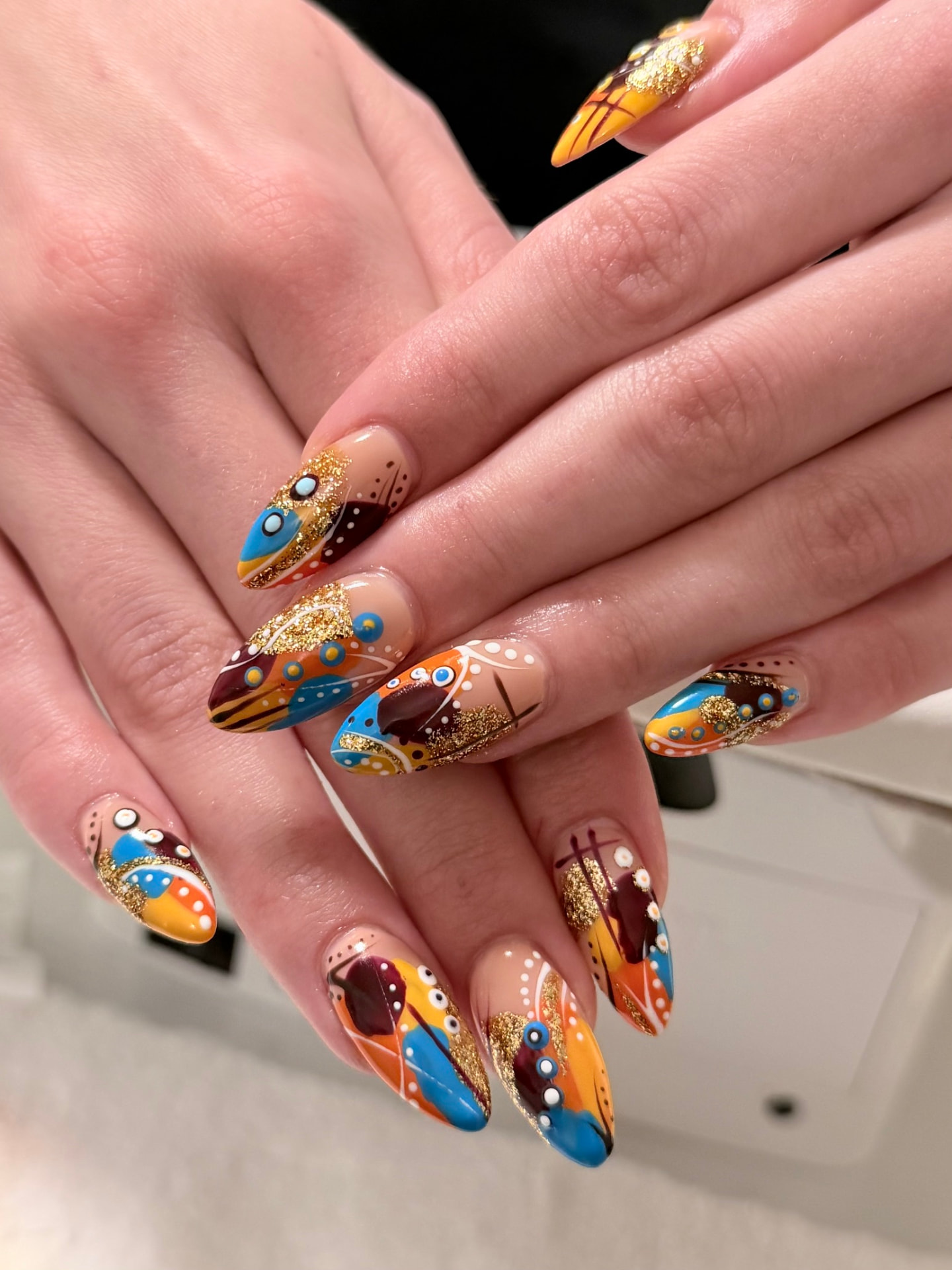 Almond nails with orange, teal, plum and gold glitter southwestern feather art
