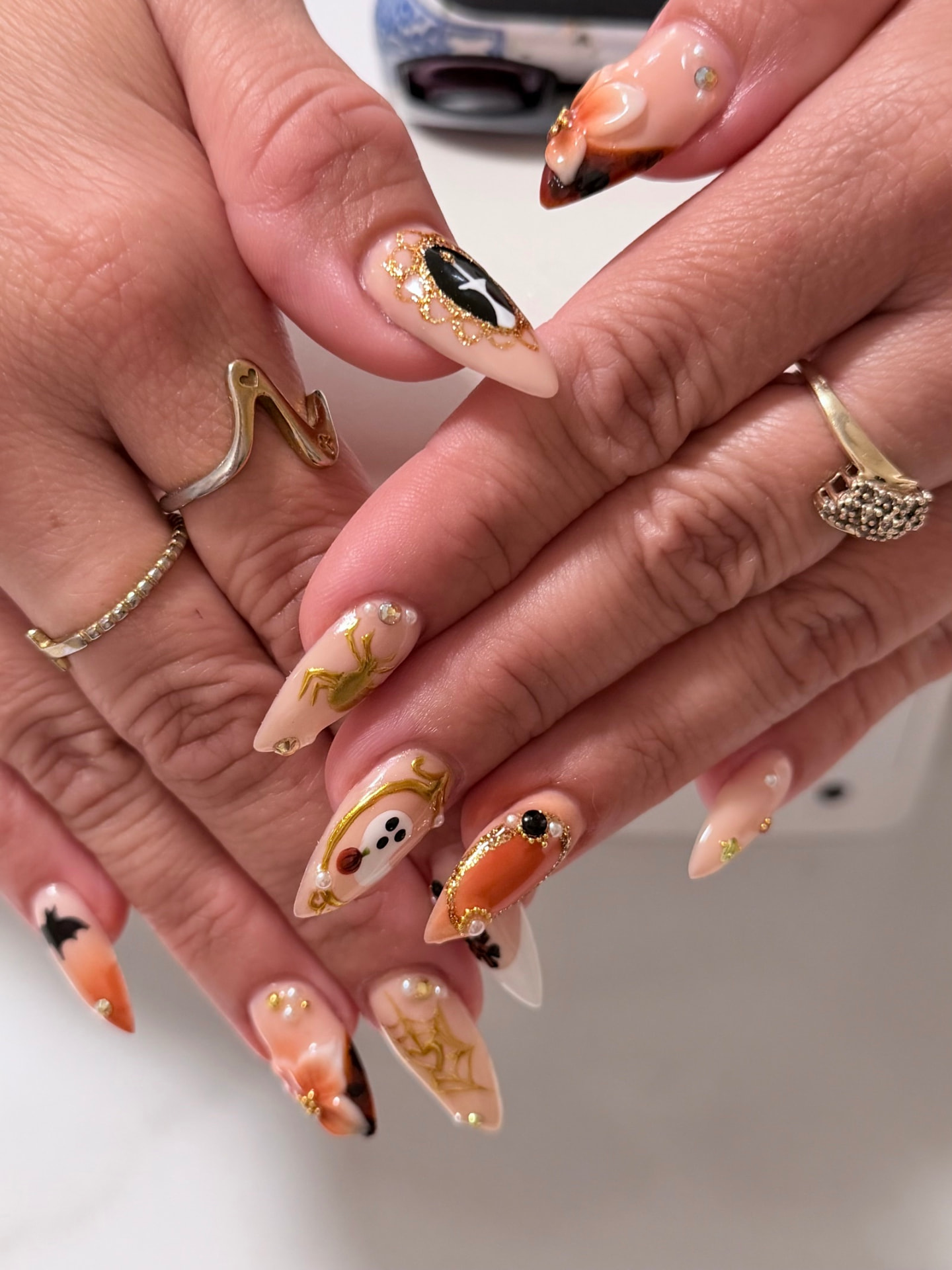 Nude stiletto nails with 3D gold spiders, webs, ghosts, pumpkins, pearls and black cat art